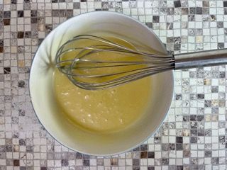 Una ciotola di liquido con una frusta dentro su un tavolo.