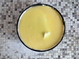 Una ciotola piena di liquido giallo è appoggiata su un tavolo piastrellato.
