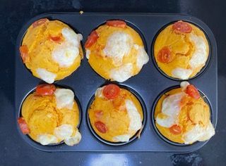 Uno stampo per muffin riempito con muffin con formaggio e pomodori sopra