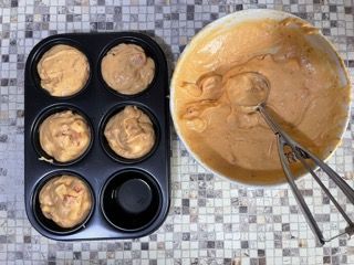 Uno stampo per muffin pieno di pastella accanto a una ciotola con la pastella.