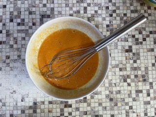 Una ciotola di salsa con una frusta dentro su un tavolo piastrellato.
