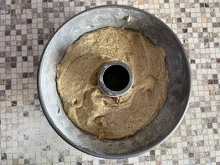 Uno stampo per ciambelle riempito di impasto è appoggiato su un tavolo piastrellato.