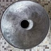 Una ciotola di metallo con un buco nel mezzo è appoggiata su un pavimento piastrellato.