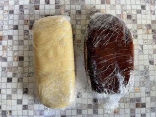 Due pezzi di pasta avvolti nella pellicola trasparente sono appoggiati su un bancone piastrellato.