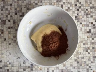 Una ciotola bianca riempita con un composto di cioccolato in polvere e zucchero a velo.