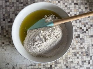Una ciotola con farina e olio e una spatola dentro.