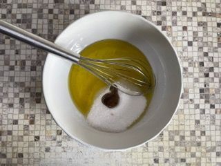 Una ciotola con olio e zucchero e una frusta dentro.