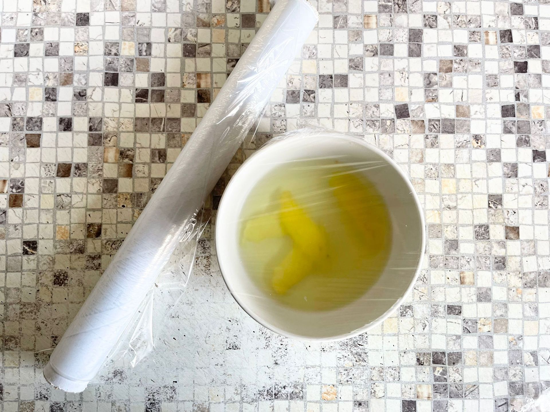 Una ciotola di liquido accanto a un rotolo di pellicola trasparente su un tavolo.