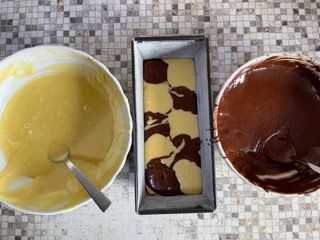 Una pagnotta di torta in una teglia accanto a una ciotola di pastella e una ciotola di salsa al cioccolato