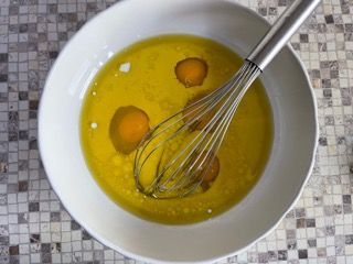 Una ciotola con uova e olio e una frusta al suo interno.