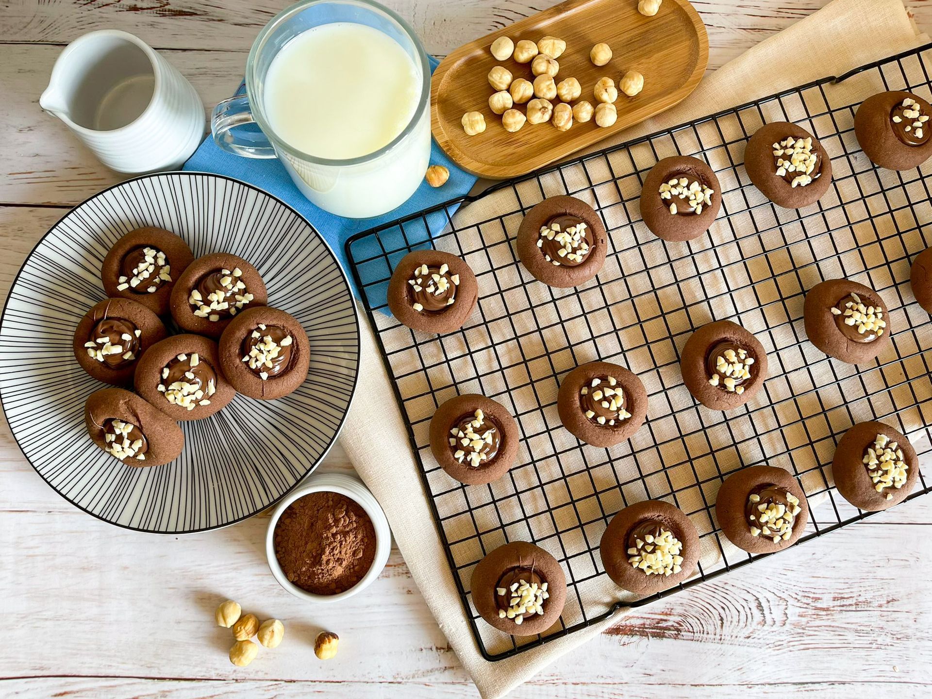 Un mucchio di biscotti al cioccolato sono appoggiati su una griglia di raffreddamento accanto a un bicchiere di latte.
