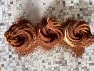 Tre cupcakes ricoperti di glassa al cioccolato sono appoggiati su un tavolo a scacchi.