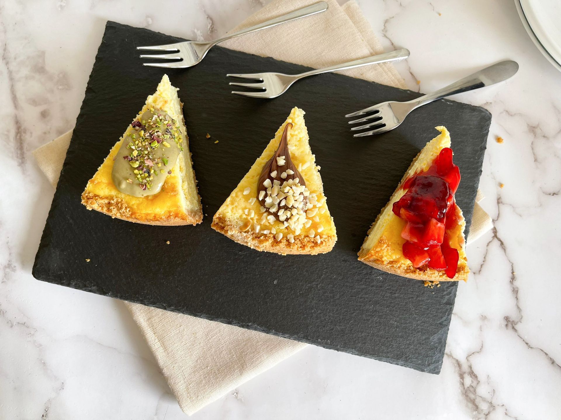 Tre fette di cheesecake su un piatto nero con forchette