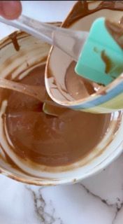 Una persona sta mescolando una ciotola di salsa al cioccolato con una spatola.