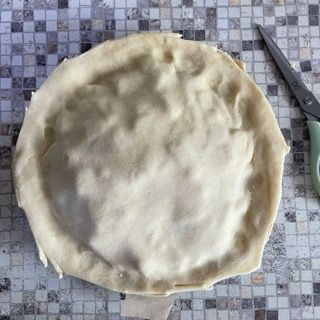 Una crosta di torta è appoggiata su un tavolo accanto a un paio di forbici