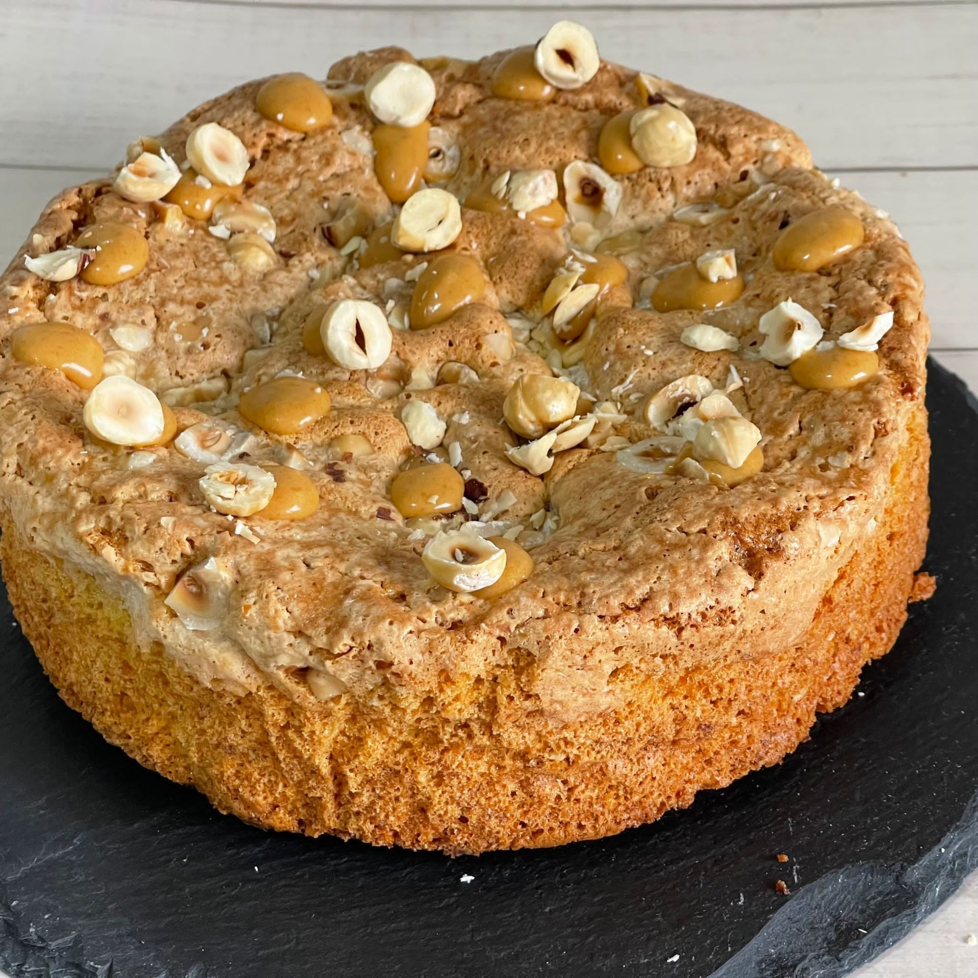 Una torta con salsa al caramello e nocciole sopra è appoggiata su un piatto nero.