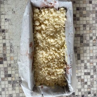 Uno stampo per plumcake pieno di briciole è appoggiato su un tavolo piastrellato.