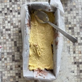 Uno stampo da plumcake pieno di pastella gialla con un cucchiaio dentro