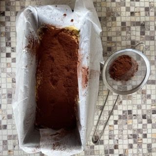 Uno stampo da plumcake riempito di cioccolato in polvere accanto a un colino.