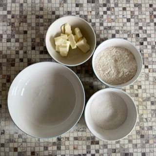 Quattro ciotole di ingredienti su un tavolo, tra cui burro e farina