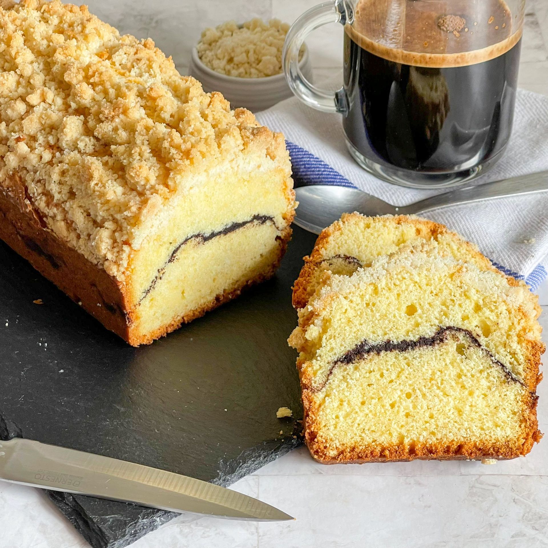 Una pagnotta di torta è appoggiata su un tagliere accanto a una tazza di caffè.