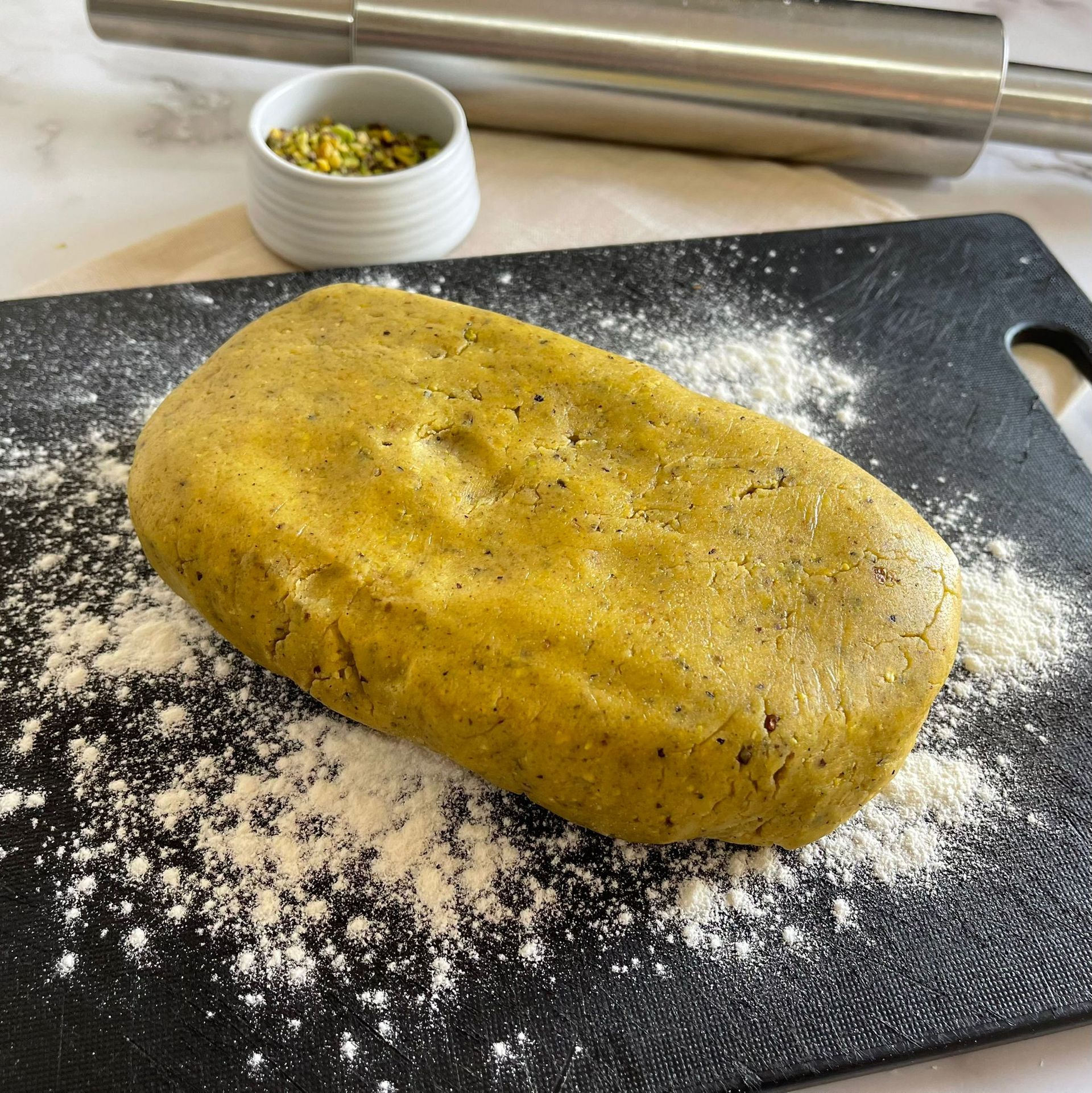 Un grosso pezzo di pasta è appoggiato su un tagliere nero ricoperto di farina.