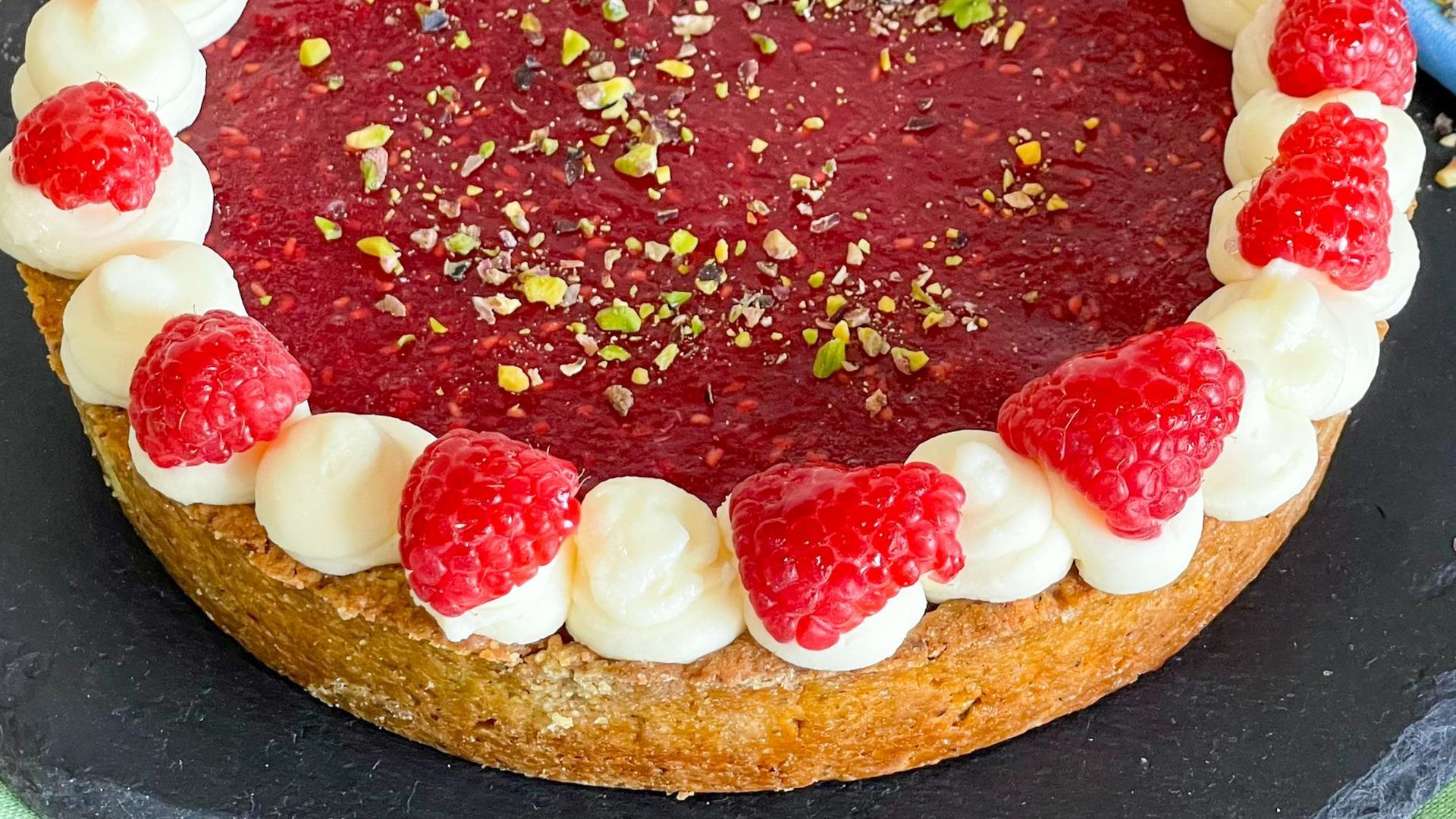 Una torta con lamponi e panna montata sopra è su un piatto nero.