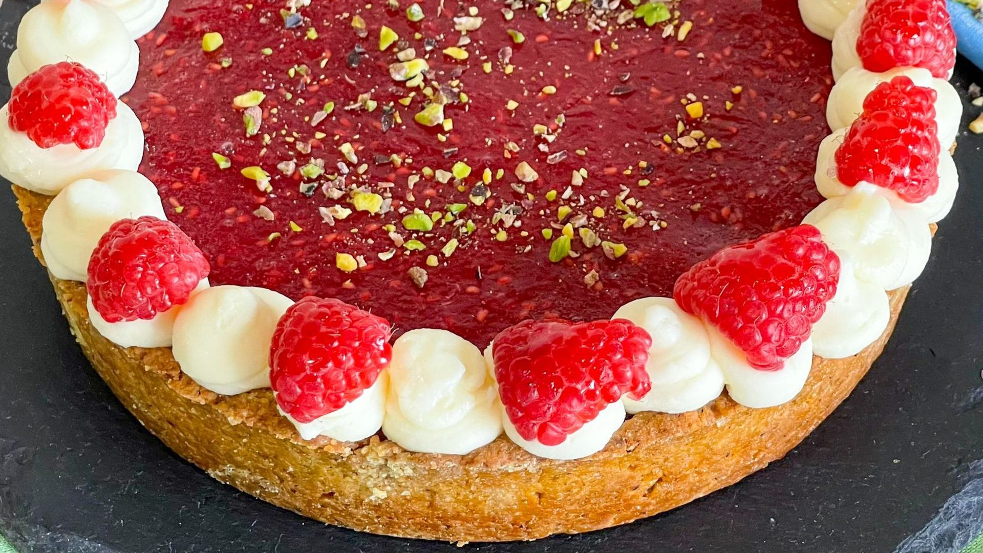 Primo piano di una torta con lamponi e panna montata sopra.