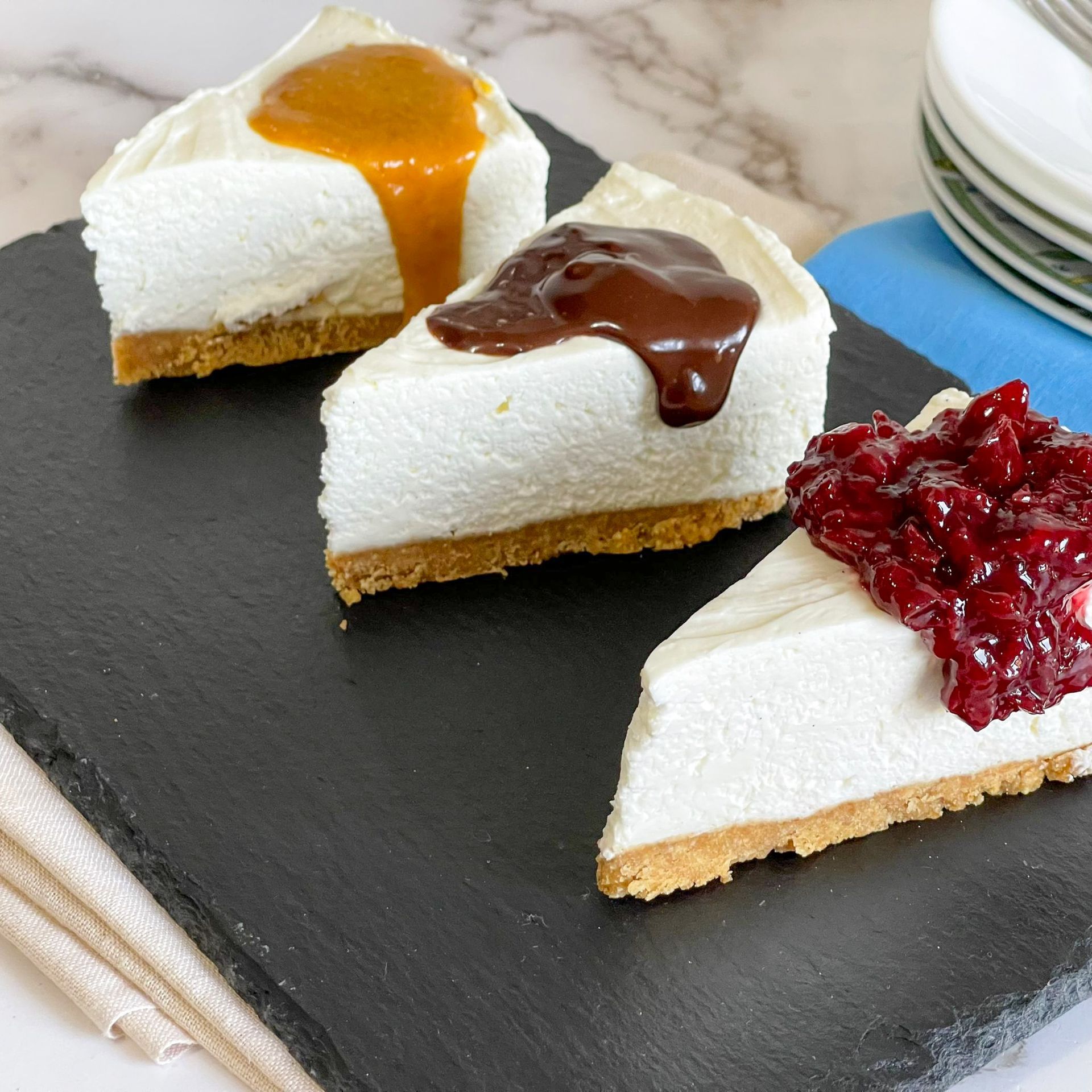 Tre fette di cheesecake con guarnizioni diverse su un tagliere nero