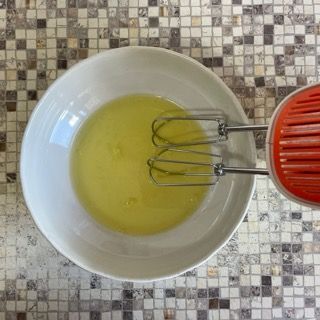 Una ciotola bianca piena di liquido giallo accanto a un mixer rosso