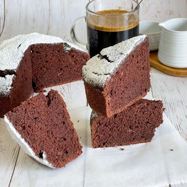 Una torta al cioccolato con zucchero a velo sopra è su un piatto accanto a una tazza di caffè.
