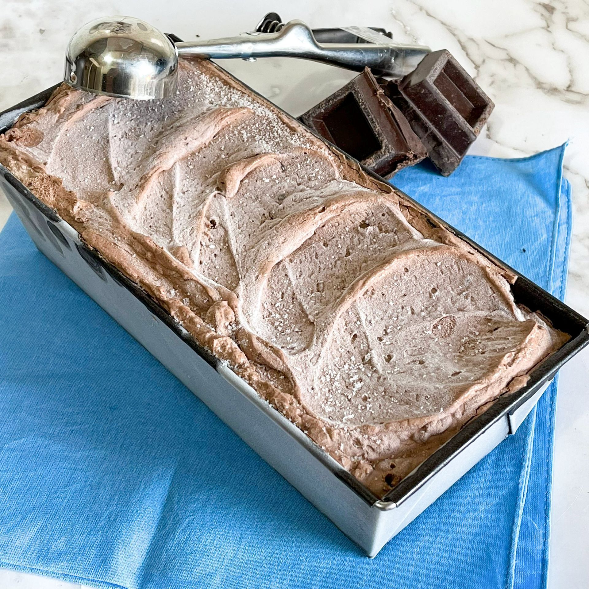 Un filone di gelato al cioccolato è appoggiato su un asciugamano blu accanto a un cucchiaio.