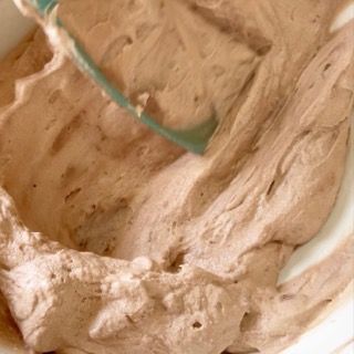 Una ciotola di glassa al cioccolato con dentro una frusta verde