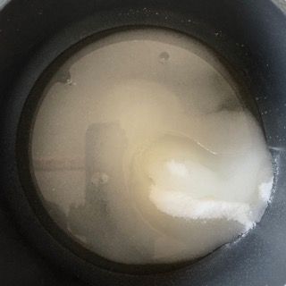 Un primo piano di un contenitore pieno di liquido con il riflesso di una persona al suo interno.