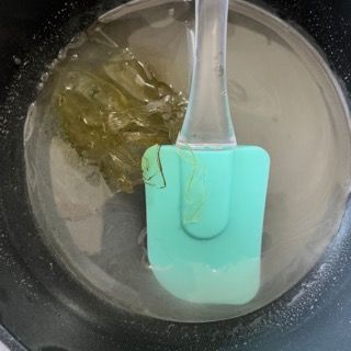 Una spatola verde è immersa in una pentola piena di liquido.