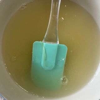 Una spatola verde è immersa in una ciotola piena di liquido.