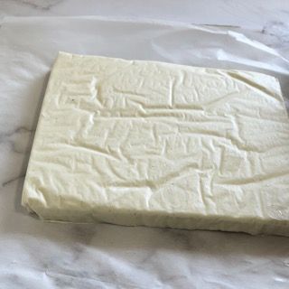 Un pezzo di formaggio è appoggiato su un foglio di carta oleata su un tavolo.
