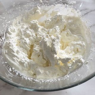 Una ciotola di vetro piena di panna montata su un tavolo.