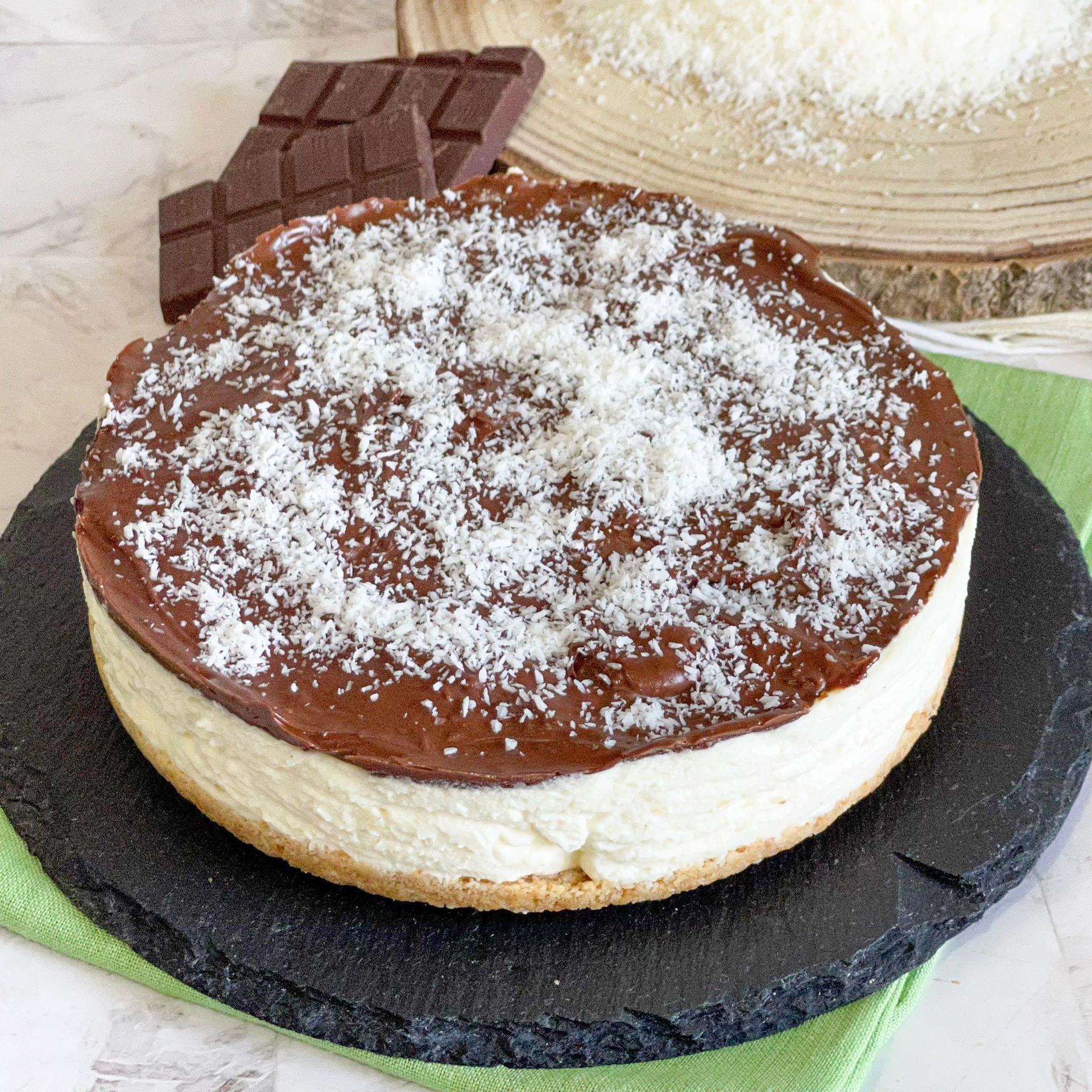 Una cheesecake con cioccolato e cocco sopra è su un piatto nero.