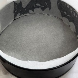 Una tortiera riempita di carta da forno è appoggiata su un tavolo.