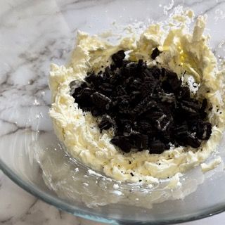Una ciotola di vetro piena di panna montata e biscotti Oreo su un tavolo.