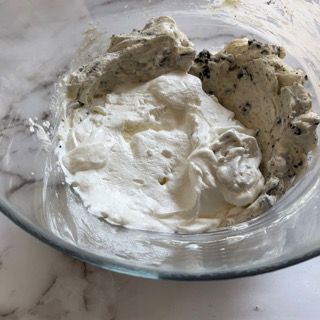 Una ciotola di vetro piena di panna montata è appoggiata su un tavolo.