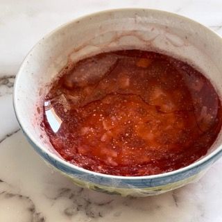 Una ciotola di marmellata di fragole è appoggiata su un tavolo.