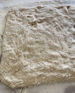 Un pezzo di pasta è appoggiato su un tavolo ricoperto di farina.