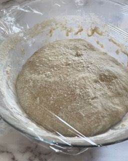 Una ciotola di impasto è coperta da pellicola trasparente su un tavolo.