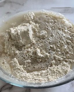 Una ciotola di vetro piena di farina e liquido su un tavolo.