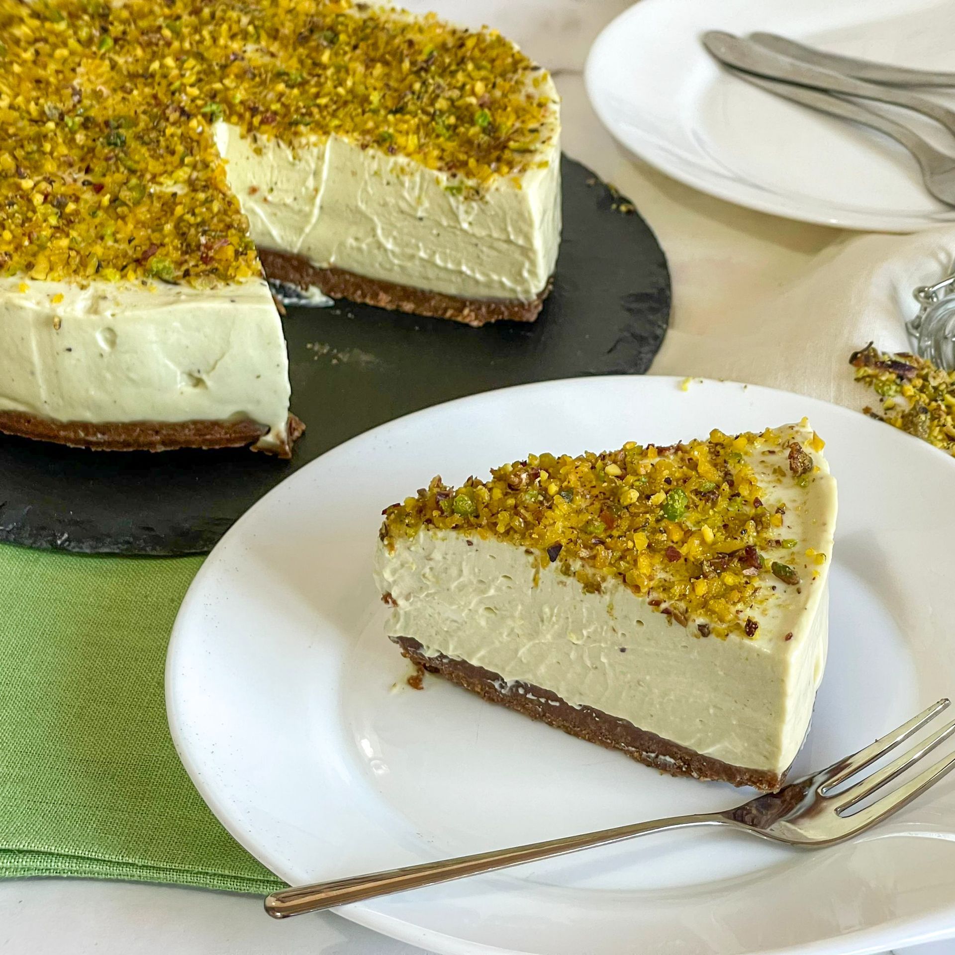 Una fetta di cheesecake con pistacchi sopra è su un piatto con una forchetta.
