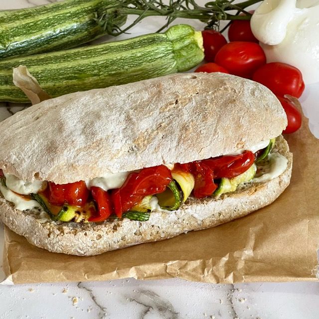 Un panino con pomodori, zucchine, peperoni e formaggio è appoggiato su un tavolo.