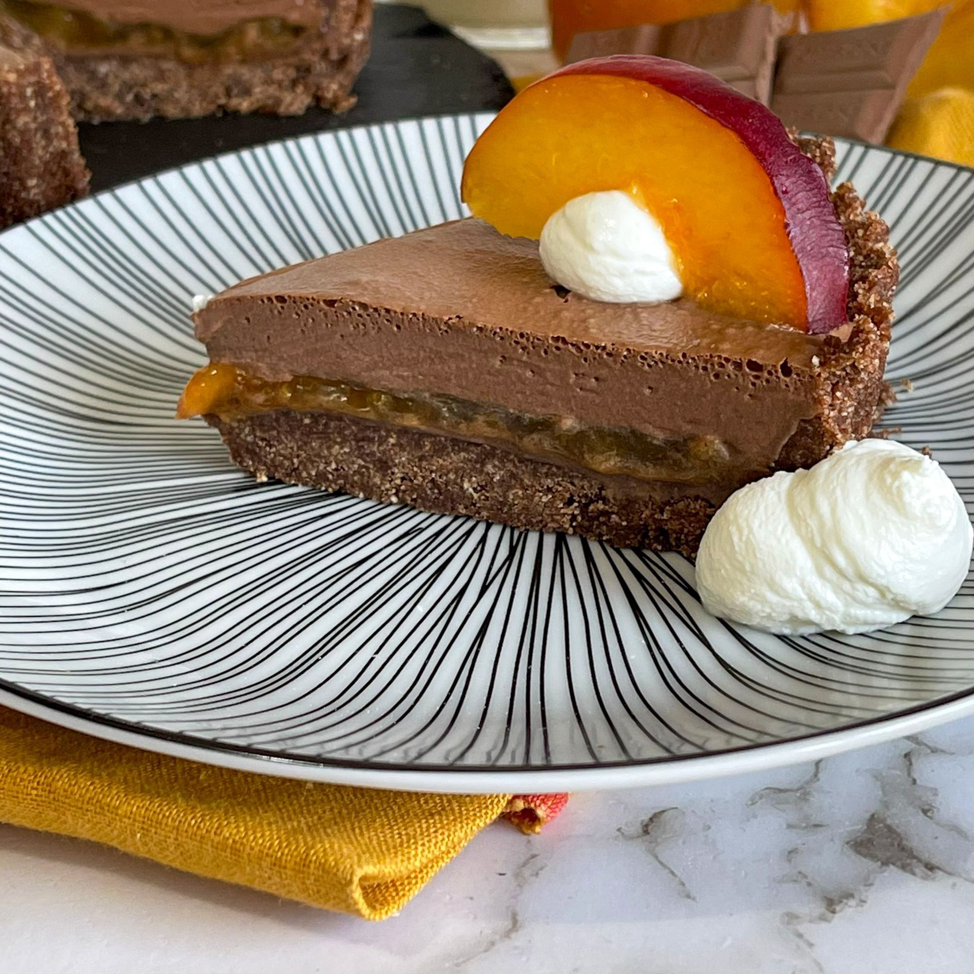 Una fetta di torta al cioccolato con panna montata e una fetta di pesca su un piatto.