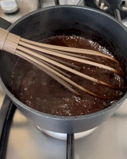 Una frusta di legno è in una pentola di salsa al cioccolato.